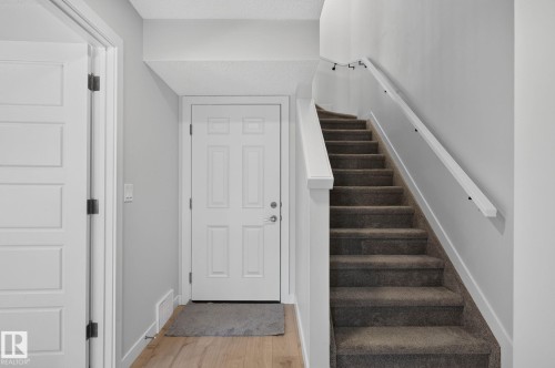 Entryway featuring wood-finish flooring, a six-panel door, and a staircase with carpeted treads and a white handrail - 33 11910 35 Avenue, Edmonton, AB 