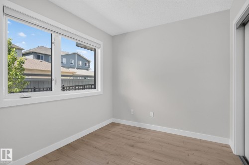 Bright room featuring a large window, neutral wall paint, wood-finish flooring, white baseboards, and a white ceiling - 33 11910 35 Avenue, Edmonton, AB 