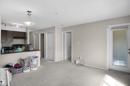 Open-concept living area with light-toned carpet flooring and a glass-paneled door - 215 1070 Mcconachie Blvd, Edmonton, AB 