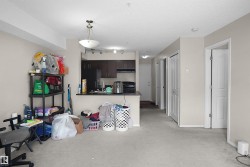 Open-concept living space featuring neutral-toned walls, light-colored carpeting, and a kitchen area with dark cabinetry, a black refrigerator, and a dark countertop - 