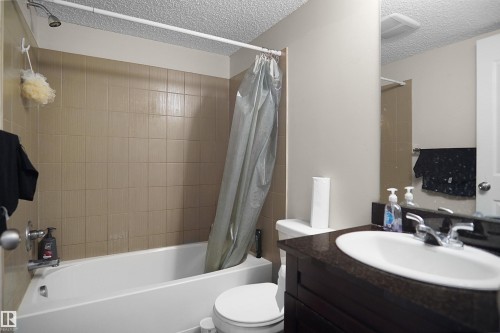 Bathroom featuring a white porcelain tub, tan ceramic tile surround, dark wood-finish vanity with an undermount sink, and a dark stone-finish countertop - 215 1070 Mcconachie Blvd, Edmonton, AB 