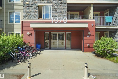 Building entrance featuring double glass doors, a stone facade, and red paneling - 215 1070 Mcconachie Blvd, Edmonton, AB 