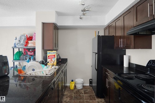 Kitchen featuring dark wood-finish cabinetry, black countertops, and a full suite of black appliances - 215 1070 Mcconachie Blvd, Edmonton, AB 
