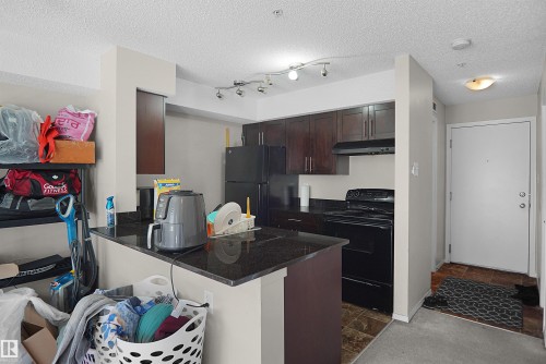 Kitchen featuring wood-finish cabinetry, black appliances, and dark granite countertops - 215 1070 Mcconachie Blvd, Edmonton, AB 