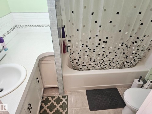 Bathroom featuring a white integrated sink, white cabinetry with dark hardware, a built-in bathtub, and a tile surround with a mosaic accent strip - 4304 121 Avenue Nw, Edmonton, AB - Indoor Photo Showing Other Room