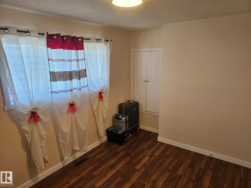 Room featuring three windows, wood-finish flooring, light-toned walls, white baseboards, and a built-in closet with double doors - 4304 121 Avenue Nw, Edmonton, AB - Indoor Photo Showing Other Room