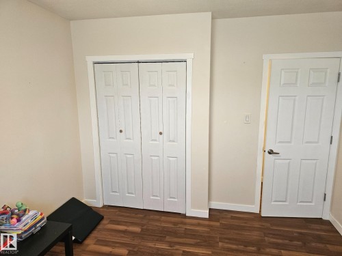 Room featuring wood-finish flooring, light-toned walls, white trim, and a white six-panel door with brushed nickel hardware - 4304 121 Avenue Nw, Edmonton, AB - Indoor