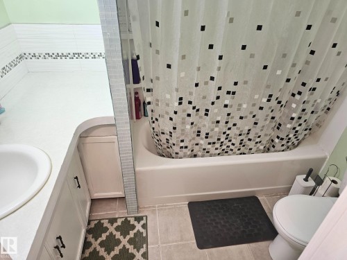 Bathroom featuring a built-in vanity with integrated sink, white cabinetry with dark hardware, a bathtub with an adjacent tiled wall niche, and light-toned floor tiling - 4304 121 Avenue Nw, Edmonton, AB - Indoor Photo Showing Other Room