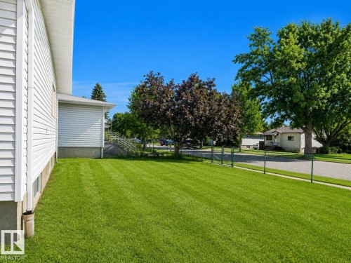 Expansive lawn area featuring a chain link fence, mature trees, and a clear blue sky - 4304 121 Avenue Nw, Edmonton, AB - Outdoor