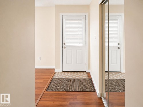 Entryway featuring a white paneled door with horizontal blinds, wood-finish flooring, and a mirrored closet door - 4304 121 Avenue Nw, Edmonton, AB - Indoor Photo Showing Other Room