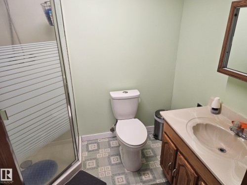 Bathroom featuring a glass-enclosed shower with frosted privacy bands, a single vanity with wood-finish cabinetry and integrated sink, a white toilet, and patterned floor tiling - 4304 121 Avenue Nw, Edmonton, AB - Indoor Photo Showing Bathroom
