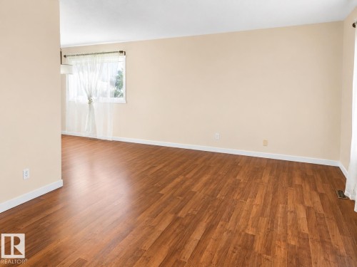 Spacious interior featuring warm-toned walls, wood-finish flooring, and white baseboards - 4304 121 Avenue Nw, Edmonton, AB - Indoor Photo Showing Other Room