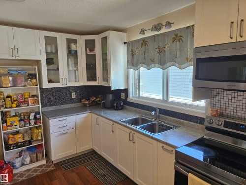 Kitchen featuring white cabinetry, a dual basin stainless steel sink, a stainless steel microwave, a built-in electric range, and a tiled backsplash - 4304 121 Avenue Nw, Edmonton, AB - Indoor Photo Showing Kitchen With Double Sink