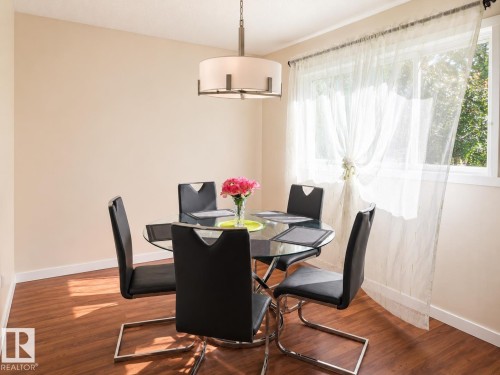 Dining area featuring wood-finish flooring, light-toned walls, and a large window with sheer white curtains - 4304 121 Avenue Nw, Edmonton, AB - Indoor Photo Showing Dining Room