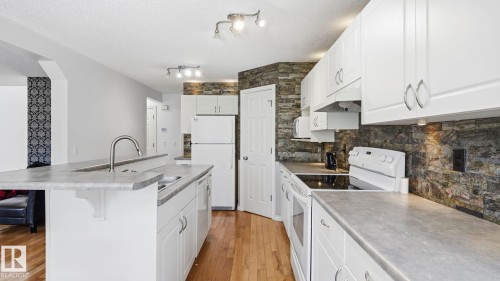 Kitchen featuring white cabinetry, stone-finish backsplash, light-toned countertops, wood-finish flooring, and track lighting - 3591 Mclean Crescent, Edmonton, AB 
