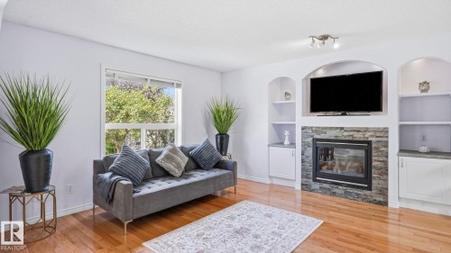 Living area featuring hardwood flooring, a large window, and a built-in media center with a fireplace - 3591 Mclean Crescent, Edmonton, AB 