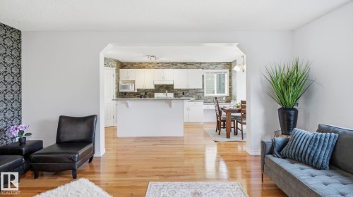 Open-concept living area with hardwood flooring, a patterned accent wall, and an arched doorway leading to the kitchen - 3591 Mclean Crescent, Edmonton, AB 