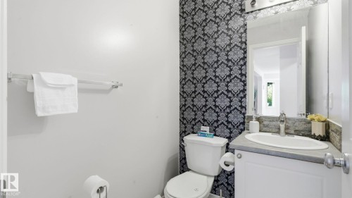 Bathroom featuring a vanity with an integrated sink, a large wall mirror, and decorative accent wallpaper - 3591 Mclean Crescent, Edmonton, AB 