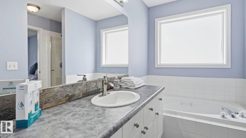 Bathroom featuring a built-in soaking tub with white tile surround, a single vanity with a white basin sink, and a large window - 3591 Mclean Crescent, Edmonton, AB 