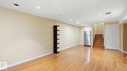 Open-concept room featuring wood-finish flooring, recessed lighting, neutral wall tones, a built-in shelving unit, and a stainless steel refrigerator - 3591 Mclean Crescent, Edmonton, AB 