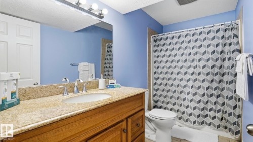 Bathroom featuring a wood-finish vanity with a built-in sink, stone-finish countertop, and wall-mounted mirror - 3591 Mclean Crescent, Edmonton, AB 