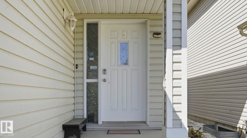 Front entry featuring a white paneled door with decorative glass insert, sidelight, and an overhead porch light - 3591 Mclean Crescent, Edmonton, AB 
