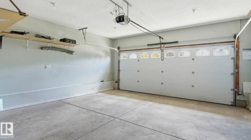 Spacious garage featuring a concrete floor, overhead lighting, an automatic garage door opener, and built-in wall shelving - 3591 Mclean Crescent, Edmonton, AB 