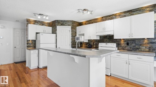 Kitchen featuring wood-finish flooring, white cabinetry, and a stone-effect backsplash - 3591 Mclean Crescent, Edmonton, AB 