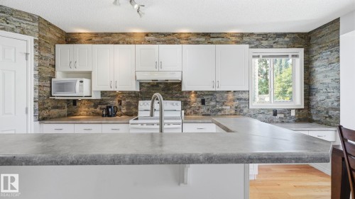 Kitchen featuring white cabinetry and a stone-look accent wall - 3591 Mclean Crescent, Edmonton, AB 