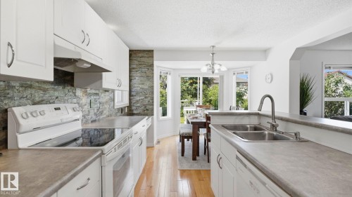 Kitchen featuring white cabinetry, stone-finish backsplash, wood-finish flooring, and a double basin sink - 3591 Mclean Crescent, Edmonton, AB 