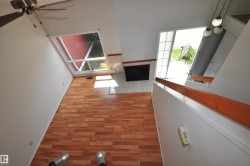 Vaulted ceiling room featuring wood-finish flooring, a large angled window, and a fireplace with a tiled hearth and surround - 