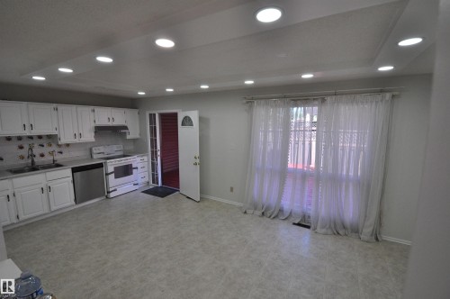 Open-concept space featuring a kitchen with white cabinetry, stainless steel dishwasher, and a white range - 617 Millbourne Road E, Edmonton, AB 