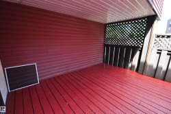 Covered outdoor space featuring red wood-finish decking and red siding - 