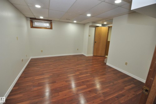 Spacious room featuring wood-finish flooring, recessed lighting, a drop ceiling, and a light-colored window with wood trim - 617 Millbourne Road E, Edmonton, AB 