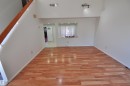 Spacious interior featuring wood-finish flooring, a light-filled window, high ceilings, track lighting, and a visible staircase with wooden railing - 617 Millbourne Road Nw, Edmonton, AB 