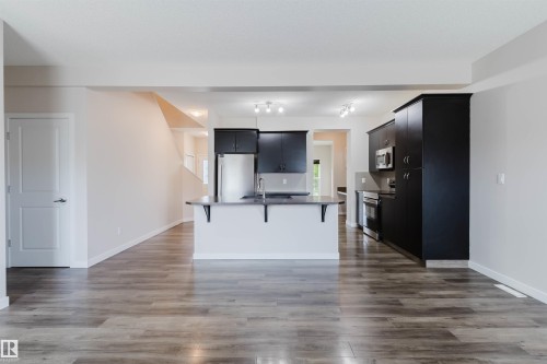 Kitchen featuring dark cabinetry, stainless steel appliances, a central island with a sink, and wood-finish flooring - 636 Mcdonough Link Link, Edmonton, AB 