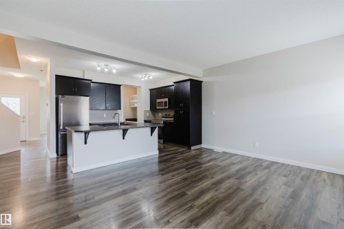 Open-concept living space featuring wood-finish flooring, a kitchen island with integrated sink, black cabinetry, stainless steel appliances, and track lighting - 636 Mcdonough Link Link, Edmonton, AB 