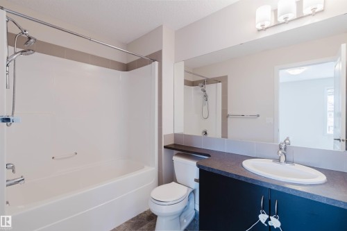 Bathroom featuring a tub/shower combination with a dual shower head, a single vanity with a dark countertop and undermount sink, a large wall-mounted mirror, and tile flooring - 636 Mcdonough Link Link, Edmonton, AB 
