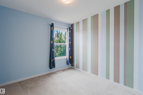 Room featuring a striped accent wall, light blue wall paint, a double-hung window, and neutral carpeting - 636 Mcdonough Link Link, Edmonton, AB 