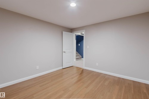 Spacious room featuring wood-finish flooring, light grey walls, white trim, and a white interior door - 636 Mcdonough Link Link, Edmonton, AB 