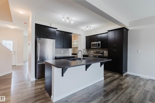 Modern kitchen featuring dark cabinetry, stainless steel appliances, and a central island with an undermount sink - 636 Mcdonough Link Link, Edmonton, AB 