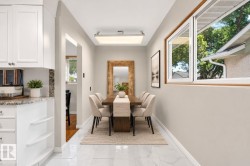 White shaker cabinetry with granite countertops, built-in shelving, and a wood-finish dining table - 