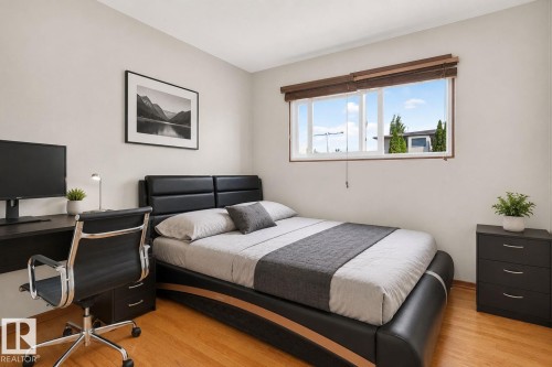 Bright bedroom featuring a large window, light-toned walls, and wood-finish flooring - 12238 48 Street, Edmonton, AB 