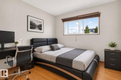 Bright bedroom featuring a large window, light-toned walls, and wood-finish flooring - 