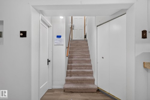 Carpeted staircase with wood railing, flanked by a white door with black hardware and white bi-fold closet doors - 12238 48 Street, Edmonton, AB 