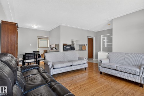 Bright living area featuring wood-finish flooring, light grey wall paint, and white crown molding - 12238 48 Street, Edmonton, AB 