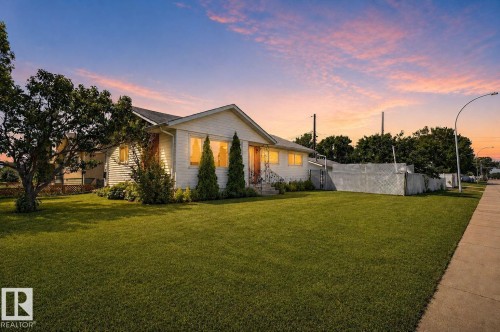 White siding exterior with a front-facing gable, featuring a manicured lawn, established trees, and a concrete sidewalk - 12238 48 Street, Edmonton, AB 