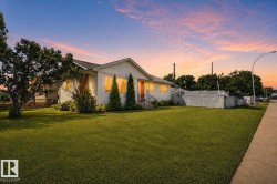 White siding exterior with a front-facing gable, featuring a manicured lawn, established trees, and a concrete sidewalk - 
