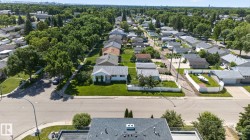 Aerial perspective showcasing a residential street with mature tree-lined sidewalks, a variety of single-story homes with pitched roofs, and manicured lawns - 