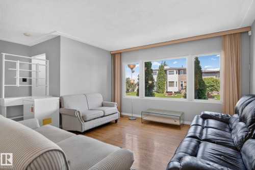 Living area featuring wood-finish flooring, a neutral wall color, crown molding, and large windows with privacy drapes - 12238 48 Street, Edmonton, AB 